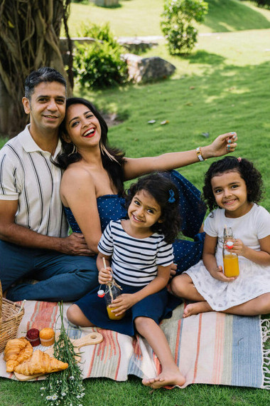 An Indian family with two girls sits on a picnic mat enjoying the outdoors