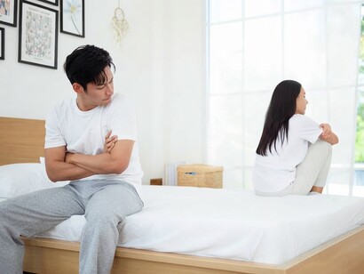 A couple sits apart in their bedroom, reflecting the emotional distance and unresolved tension between them