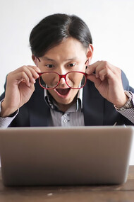 An entrepreneur looking at his laptop with surprise and happiness