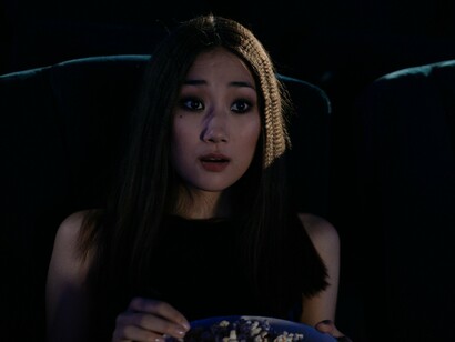 Uma espectadora segura um balde de pipoca e reage com surpresa enquanto assiste a um filme em uma sala escura. No cinema, as imagens e as histórias despertam emoções que nos aproximam de experiências humanas muito diferentes das nossas