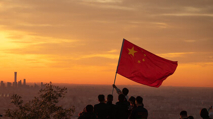 A group of people stands atop a hill, proudly holding the flag of China, with Beijing in the background
