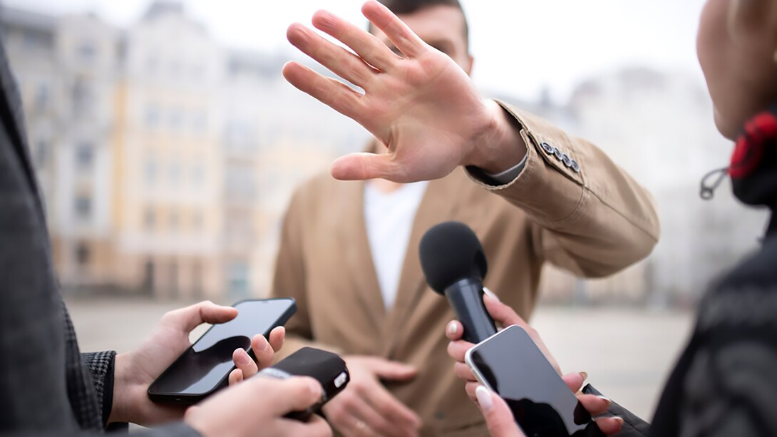 A close-up image of a reporter conducting an interview, with a person gesturing to block the camera
