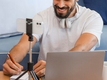 A content creator at home, multitasking between vlogging and managing social media on his laptop