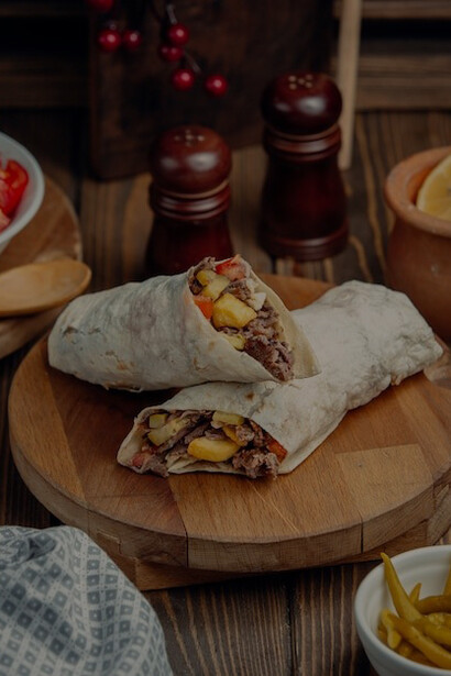 A side view of shawarma served with crispy fried potatoes, a refreshing glass of ayran, and a side of mayonnaise on a wooden board—classic Turkish doner kebab