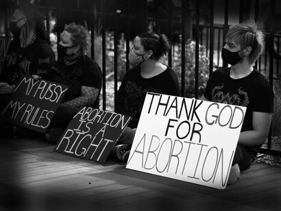 White protestors echoing the sentiment of anti-abortion are sitting with their respective signs peacefully while wearing masks