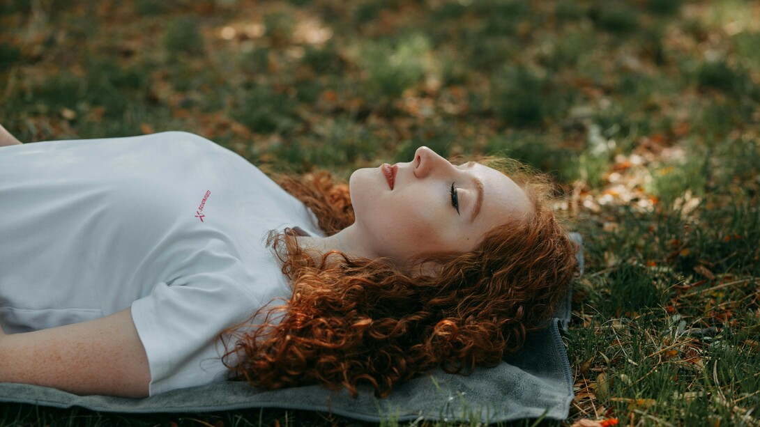 A moment of tranquility: a young woman with vibrant red hair rests on a soft blanket amidst the lush green grass