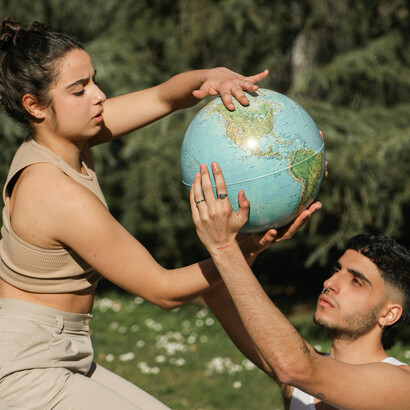 A couple posing with a globe in a lush natural setting, symbolizing harmony, coexistence, and humanity’s deep connection to the Earth