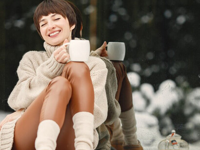 A young woman in a white sweater sips tea while enjoying the beauty of nature in winter