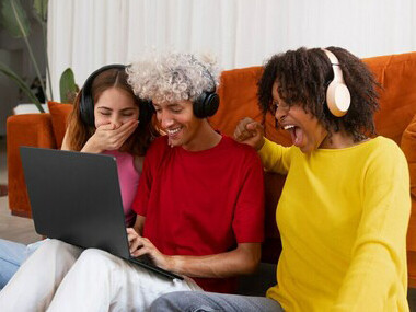 Friends watching videos on a computer in a medium shot, showcasing the role of digital platforms and social media in shaping global communication