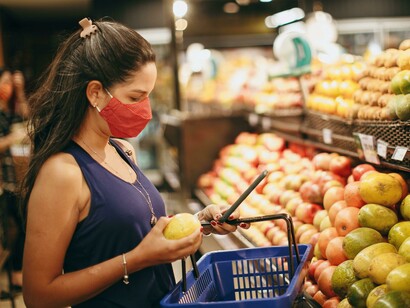 A woman checks grocery prices on her phone while shopping, highlighting the strain of rising living costs on everyday consumers