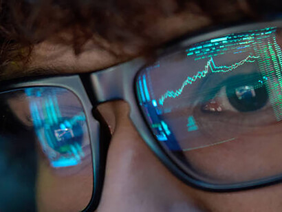 Amid the era of digitalism, a young business man gazes at a computer screen, with its vibrant reflections illuminating his glasses, emblematic of the pervasive influence of technology in every facet of modern life