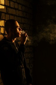 A man leaning against a wall smoking a cigarette 
