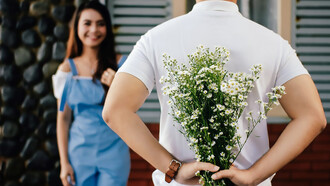 A man stands before a woman near a marble wall, tenderly presenting a bouquet of flowers, creating a scene of timeless romance