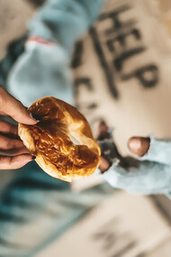 A person begging under a bridge receiving bread from another individual, highlighting acts of generosity, reciprocity, and kindness in giving and receiving