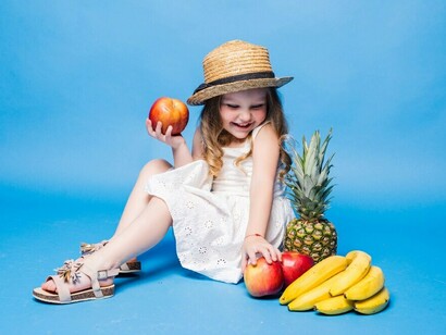 A young child holding fresh vegetables in front of a blue background, discovering how to make healthy food decisions