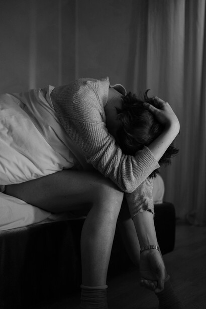 A person sits alone with a blanket, holding her head as she appears anxious and deep in thought