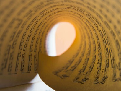 Foglio di spartito avvolto a spirale: “Uno dei primi a formalizzare il rapporto tra numeri e musica fu Pitagora. Si narra che scoprì l’armonia osservando il suono prodotto da corde di diversa lunghezza”