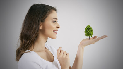 A woman gently holds a growing tree in her hand, symbolizing care for nature and growth