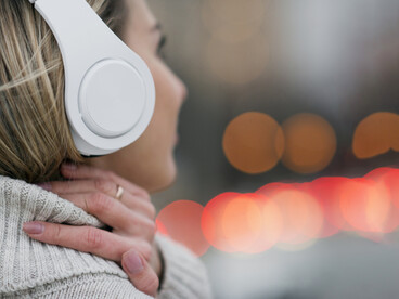 From behind, a woman holds her headphones while taking in the rooftop view