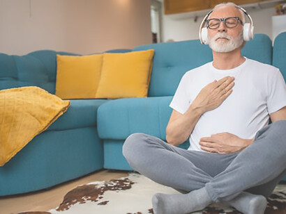 An elderly gentleman engages in a serene moment of guided meditation within the comfort of his home, seated gracefully on the floor, embodying the essence of relaxation for both body and mind