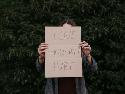 A woman covering her face with the sign "love should not hurt"
