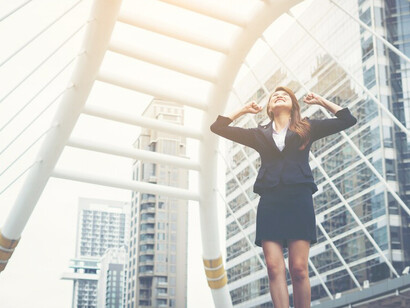 Happy and successful businesswoman with raised hands in a dark suit overlooking the city center, symbolizing career development and professional success