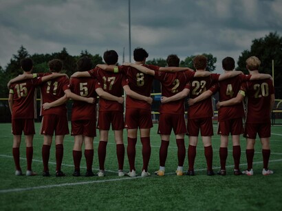 A college Men's Soccer team locked in arms as they hear the USA national anthm