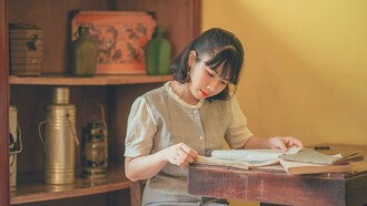 A woman carefully reading aged books at a wooden desk, representing the lifelong pursuit of knowledge through dedicated reading