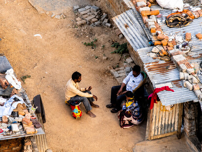 People wearing face masks gather outside makeshift homes in a densely populated informal settlement in the Global South