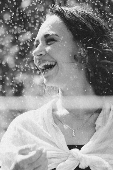 A grayscale photo of a happy woman laughing in the rain