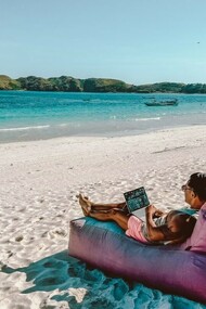 A man sitting on a bean bag on the beach, working on his laptop in Lombok