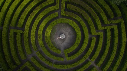 A person standing at the heart of a vast maze, symbolizing humanity’s struggle to maintain direction during times of uncertainty
