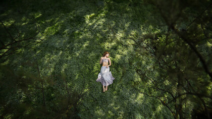 A girl lies on the grass in a garden, viewed from above, lost in quiet reflection