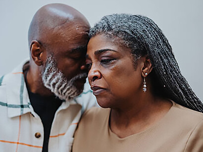 A senior man holds his wife’s hand and comforts her as she breaks down during her cancer journey