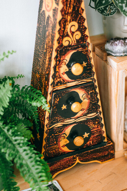 Detailed view of a decorative wooden box with celestial moon and star motifs, surrounded by plants