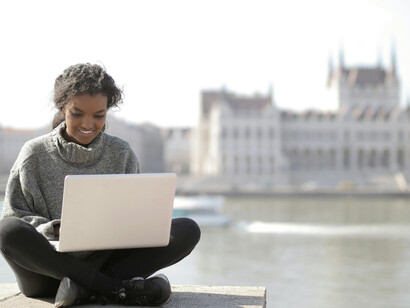 A woman in a gray long-sleeve shirt works remotely outdoors in a European city, enjoying the digital nomad lifestyle