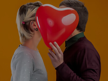 A Valentine's Day-themed image captures a young couple joyfully hiding their faces behind a heart-shaped balloon, symbolizing love and affection