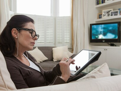 Una mujer manejando su tablet y sin prestar atención a la televisión encendida
