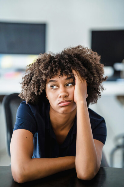 Portrait of a woman at a desk resting her face on her hand, appearing tired and lost in deep thought
