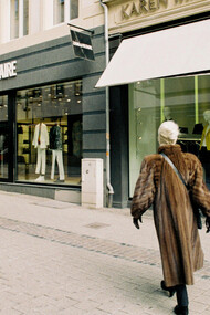 Stylish woman in a brown fur coat passing by the storefronts of high-end brands such as Zadig & Voltaire