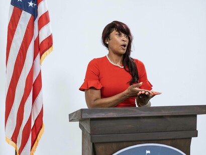 A woman behind a podium is addressing the room with her public speaking skills