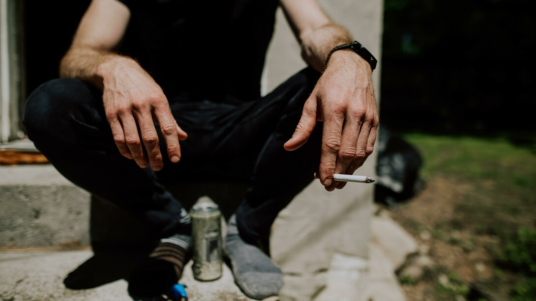 A person sitting on a step with a can and a cigarette 