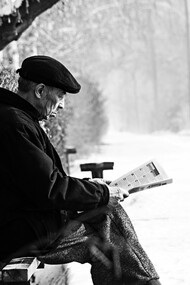 Velhinho sentado na praça lendo jornal no inverno
