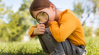 A small girl is using a magnifying glass to explore her surroundings and solve problems