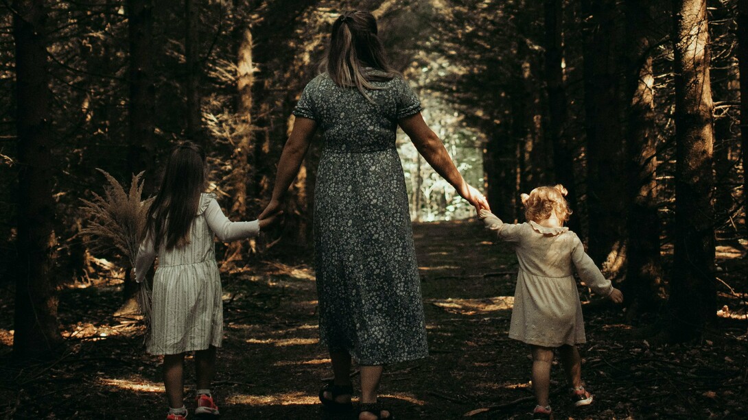 Hand in hand, they move forward — a quiet moment of safety and belonging beneath the trees