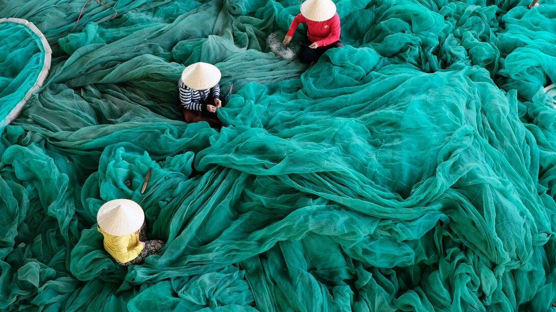 Donne vietnamite che lavorano alla realizzazione di una grande rete verde
