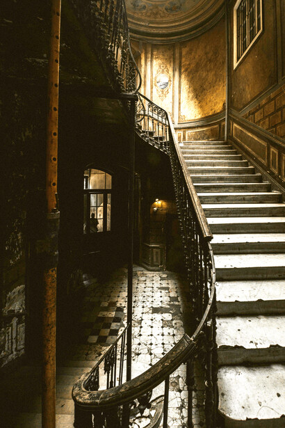 A dark, decaying house interior, with broken floor tiles scattered near the staircase