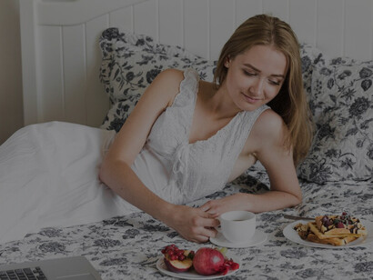 A young woman enjoys a healthy breakfast in bed, highlighting the connection between sleep, diet, and nutrients for improved sleep quality
