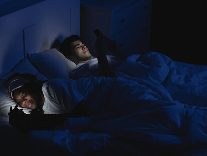 A woman using her mobile phone while lying on a bed