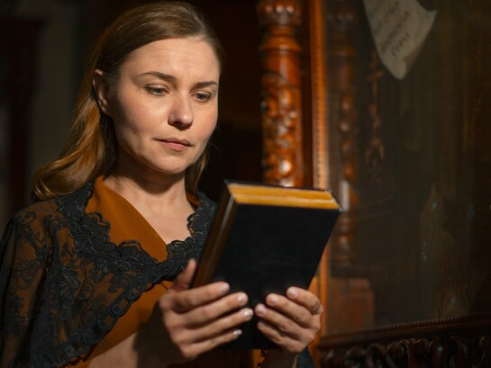 A reader holding an ancient religious manuscript, representing the preservation of Katharevousa through religious practice